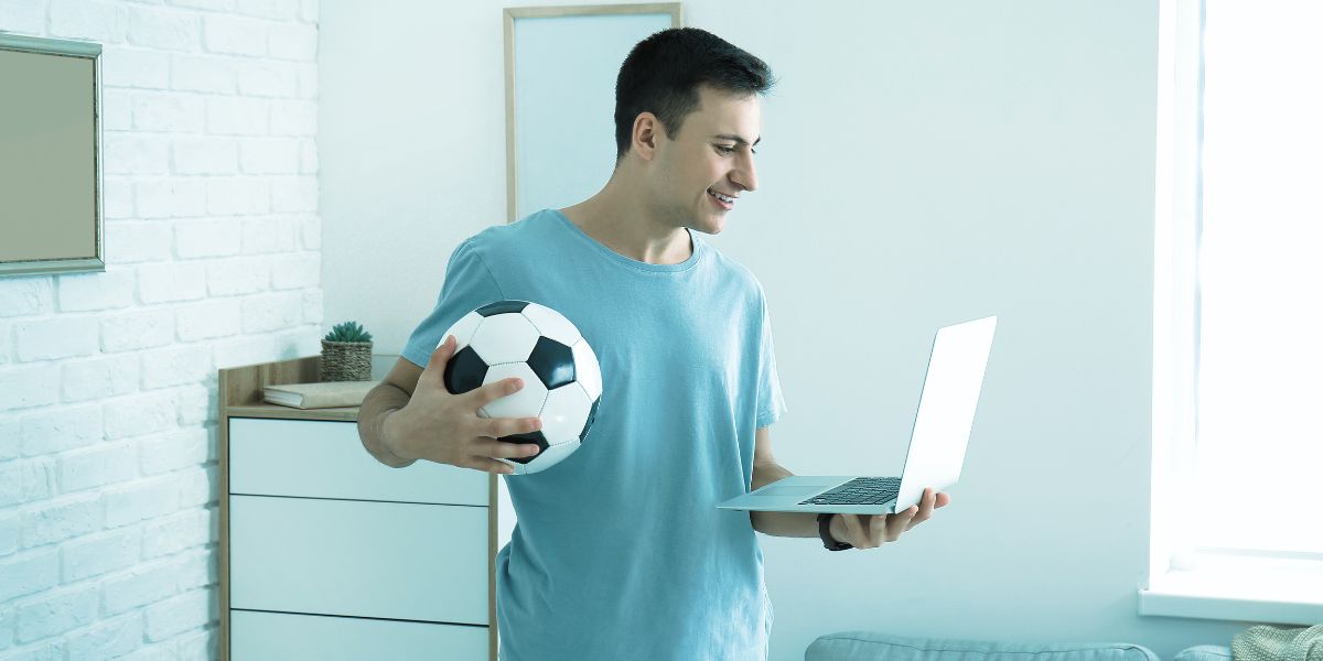 homme qui tient son ordinateur à la main et qui regarde un match - Le Bon Parieur